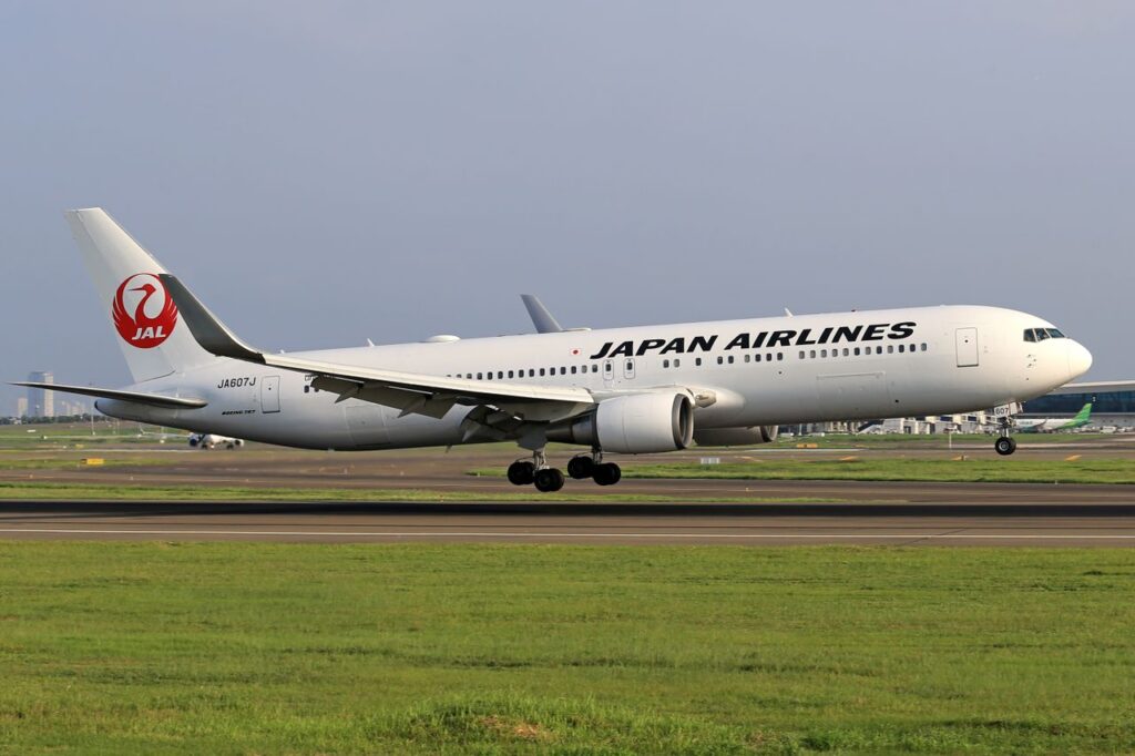 A Japan Airlines airplane landing on a clear day with airport in the background.